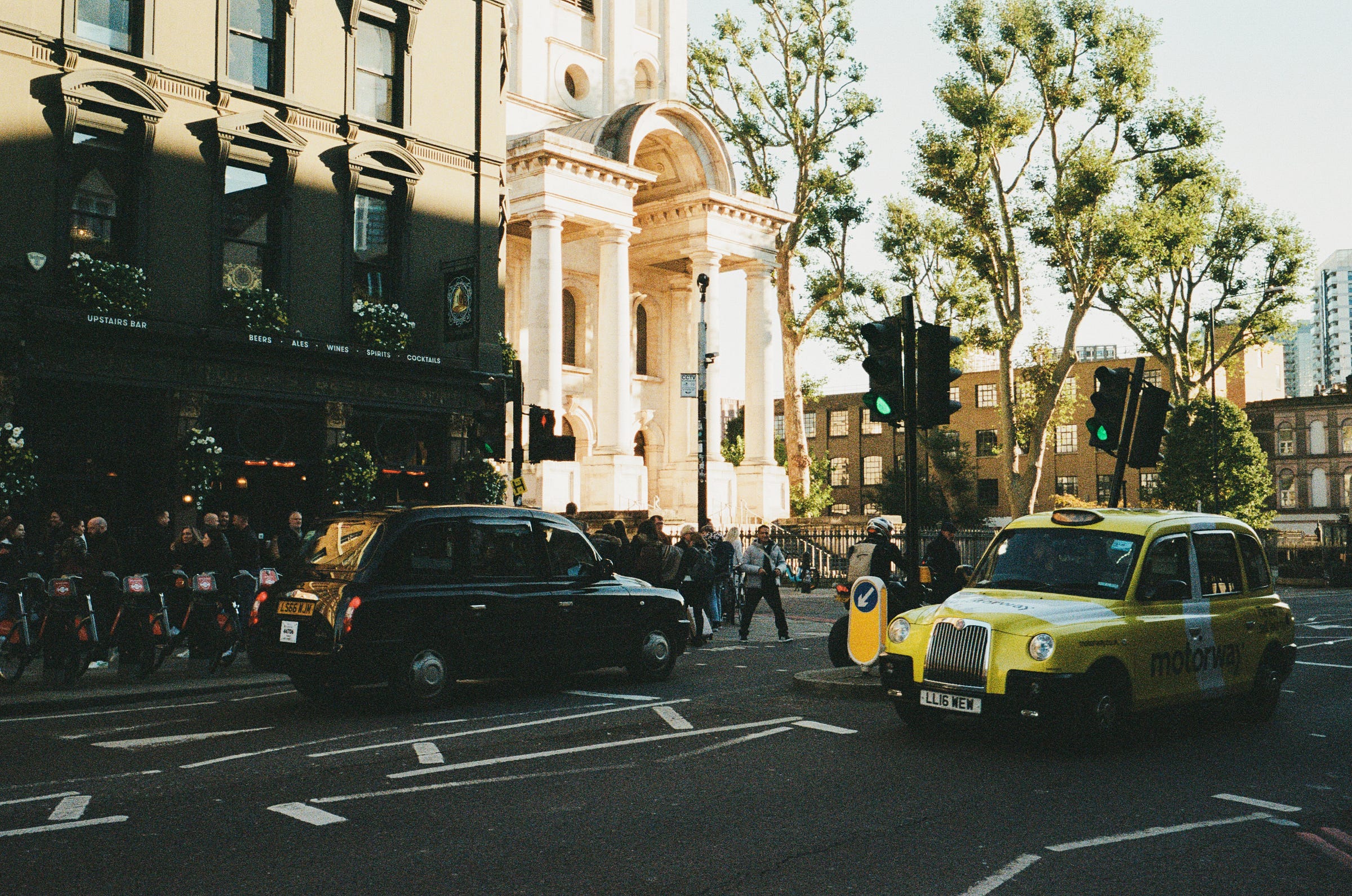 Two taxis reflect their backgrounds as they pass each other. London 2023
